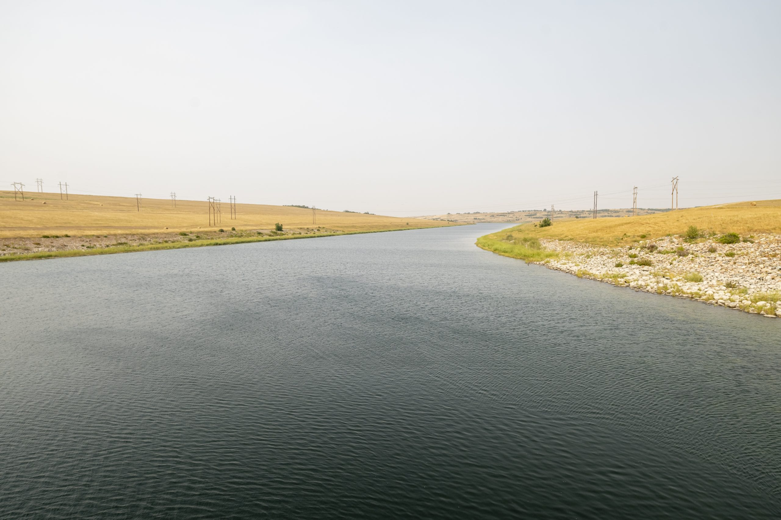 A river flows between two fields with power lines on either side